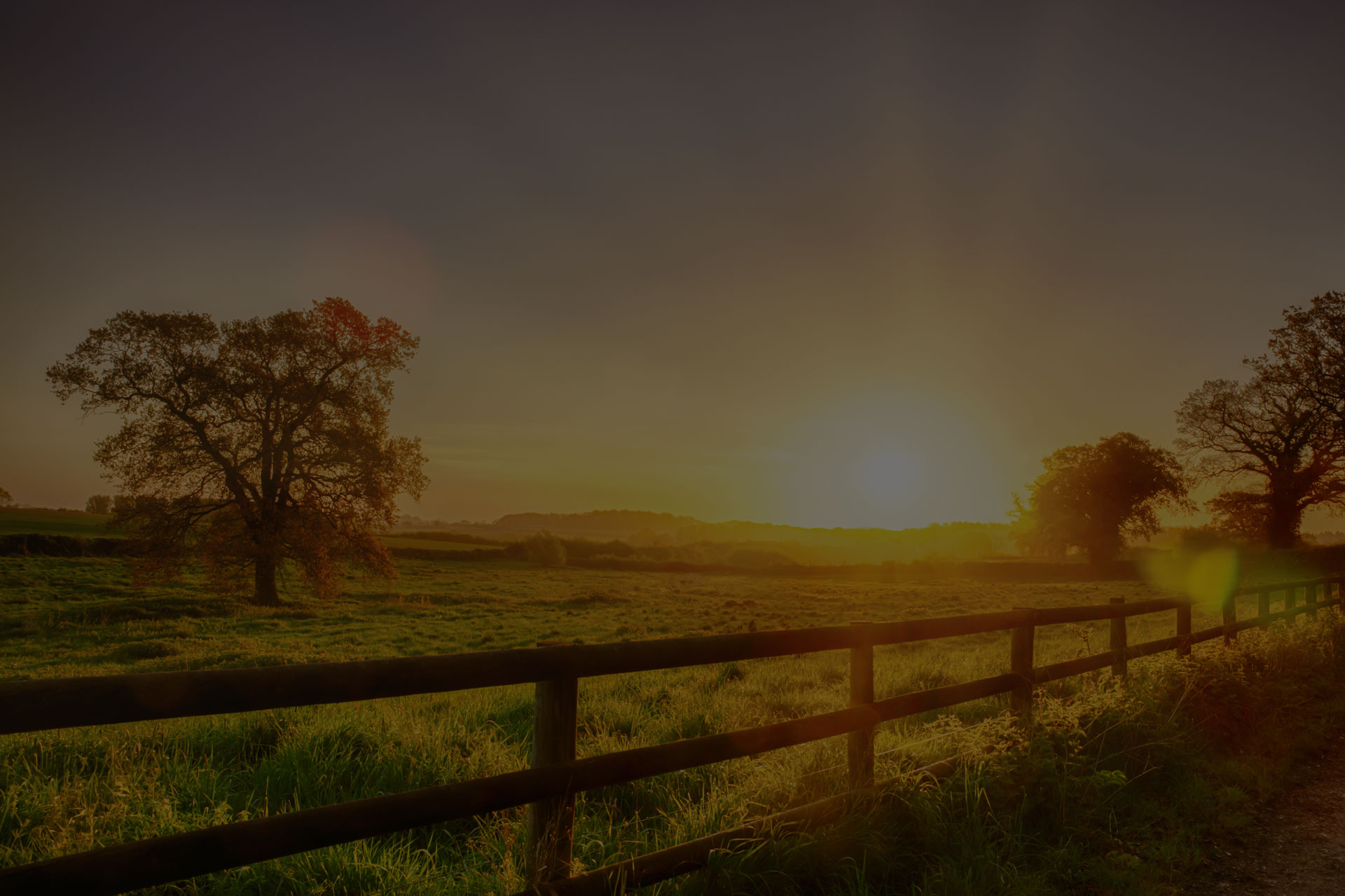 Glorious sunrise over grassy rural landscape in Norfolk UK with a two bar fence disappearing off into the distance. - Image